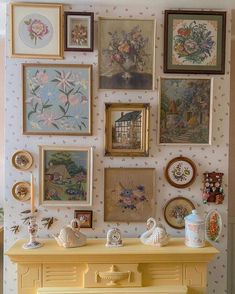 there are many framed pictures on the wall next to a yellow table with vases