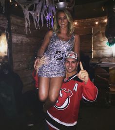 a man standing next to a woman on top of a skateboard in front of a wooden wall