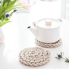 a white tea pot sitting on top of a table next to a roped coaster