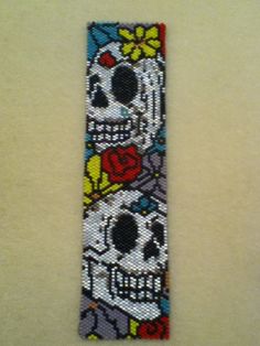 a beaded bookmark with a skull and roses on the front, sitting on a white surface