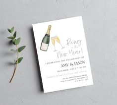 a wine bottle and two glasses of champagne on top of a white card with greenery