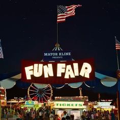 the fun fair is lit up at night with american flags flying in the sky above it