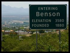 a street sign on the side of a road near some trees and mountains in the background