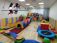 two children playing in a play room with colorful walls and flooring, while one child is on a trampoline suspended from the ceiling