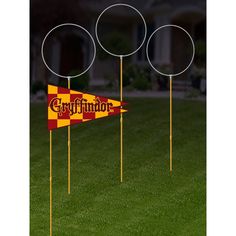 three yellow and red flags are in the grass near some round poles that say gryffindor