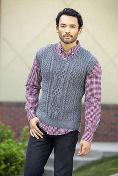 a man standing in front of a building wearing a gray sweater vest and black pants