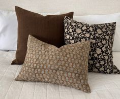 four decorative pillows on a bed with white linens and brown trim around the edges