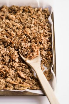 a pan filled with granola on top of a white table next to a wooden spoon