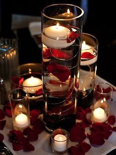 candles and rose petals are arranged in glass vases on a table with red roses