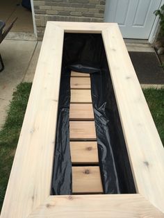 an unfinished wooden bench with black tarp on the bottom and one piece of wood sticking out of it