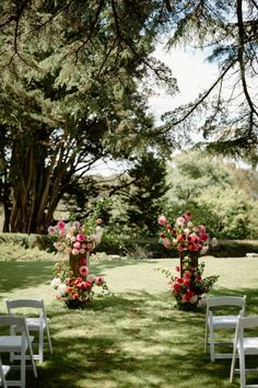 two white chairs sitting on top of a grass covered field next to flowers and trees