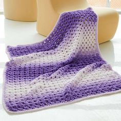 a purple and white crocheted blanket sitting on top of a table next to a vase