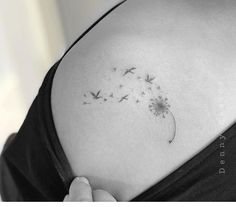 a black and white photo of a woman's back shoulder with a dandelion tattoo