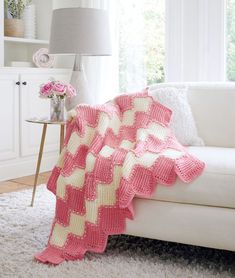 a living room with a white couch and pink crocheted blanket on top of it