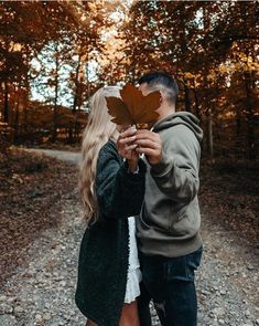 a man and woman holding up a leaf in the middle of a road with trees behind them