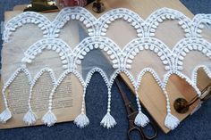 white lace with tassels and scissors sitting on top of a piece of paper