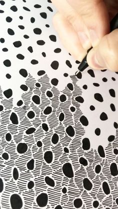 a person using a pen to draw on a piece of paper with black and white dots