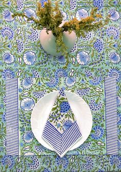 a blue and white table cloth with flowers in vases next to it on a plate