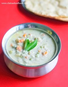 a silver bowl filled with food on top of a red table next to pita bread