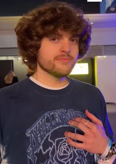 a man with curly hair wearing a blue t - shirt and looking at the camera