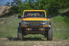 the front end of a yellow truck parked on top of a grass covered field with trees in the background