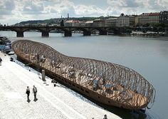 a large wooden structure sitting on the side of a river next to a bridge and buildings