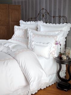 a bed with white comforter and pillows on it next to a night stand in front of a striped wall