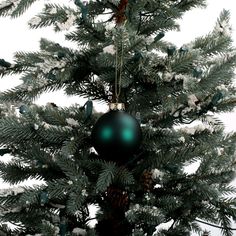 a green ornament hanging from the top of a pine tree with snow on it