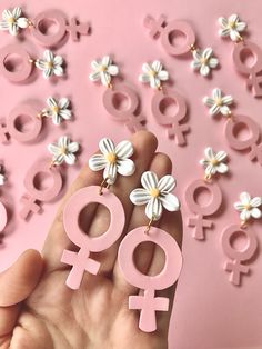 a person holding pink and white earrings with flowers in the shape of women's heads