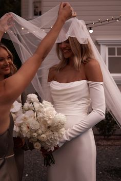 two women in white dresses and veils are smiling at each other as they hold bouquets