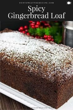 a loaf of spicey gingerbread loaf on a white plate with red berries in the background