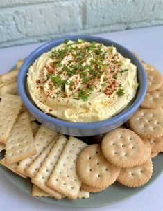 a bowl of hummus with crackers on the side and garnished with chives