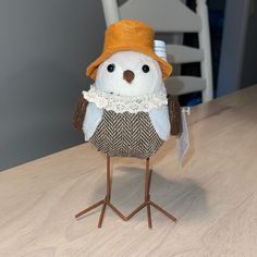 a small stuffed animal wearing a hat and scarf on a wooden table with a white chair in the background