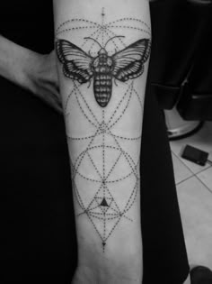 a black and white photo of a moth tattoo on the left inner arm, with geometric shapes around it