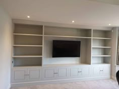 an empty living room with white bookcases and a flat screen tv mounted on the wall