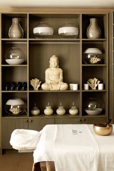 a buddha statue sitting on top of a wooden shelf filled with bowls and plates next to a white bed