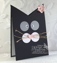 a black card with a cat's face on it and a pink flower in the middle