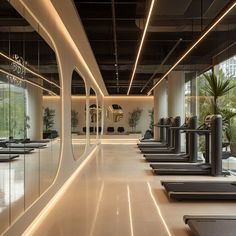 a row of treadmills in a gym with mirrors on the wall and windows