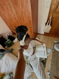 a woman sitting on the floor with headphones in her ears and reading a book