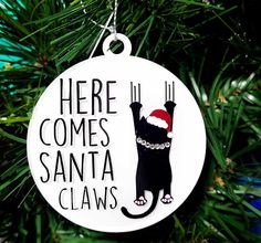 a christmas ornament with a black cat wearing a santa hat and saying here comes santa claws