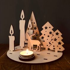 a candle is lit in front of some paper cut out trees and candles on a table