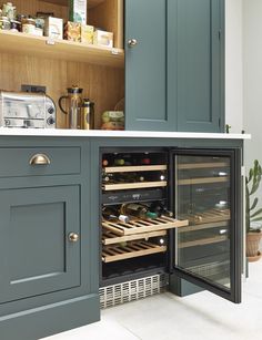 an open wine cooler in the corner of a kitchen with blue cabinets and white countertops