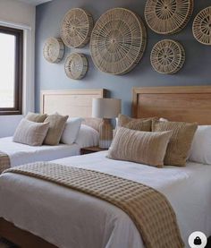 two beds in a room with wicker baskets on the wall above them and windows