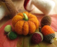 small felted pumpkins and acorns sitting on top of a fall leaf