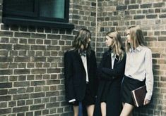 three young women standing next to a brick wall