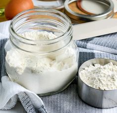 a glass jar filled with white flour next to two measuring spoons on a towel