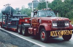 a red tow truck driving down a road next to power lines and trees in the background