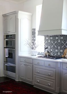 a kitchen with white cabinets and black tile backsplash, an oven and range hood