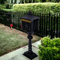 a black mailbox sitting on the side of a sidewalk next to a lush green field