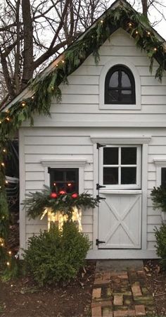 a white house with christmas lights on the windows and wreaths hanging from it's roof